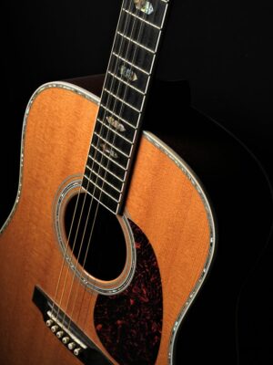 Close-up view of an acoustic guitar against a black background, highlighting its strings and body.