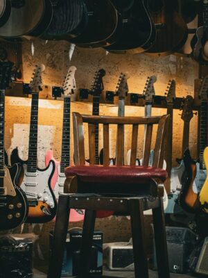 A cozy music store with a variety of guitars on display and a single chair in the center.