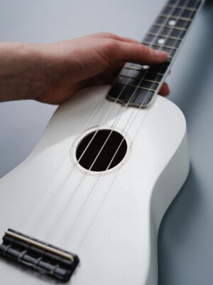 A hand strumming a white ukulele with focus on the strings and finger placement.